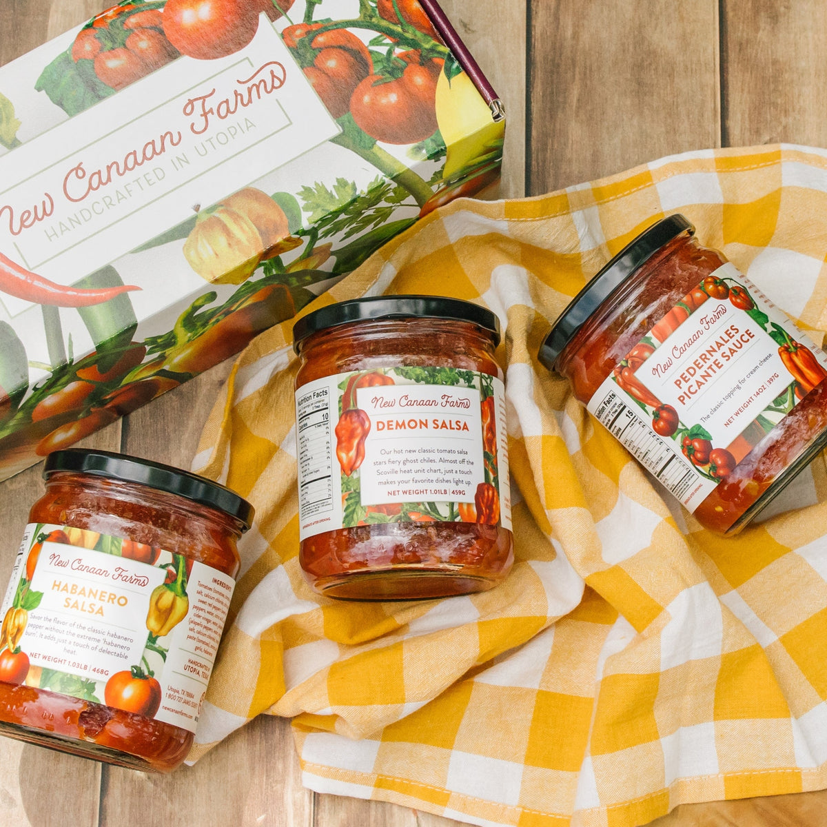 Habanero Salsa, Demon Salsa and Pedernales Picante Sauce on a yellow checked cloth beside a New Canaan Farms gift box