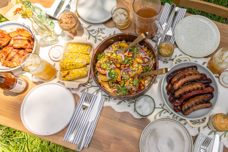 Backyard table set with grilled chicken, corn on the cob, a peach salad and sausages