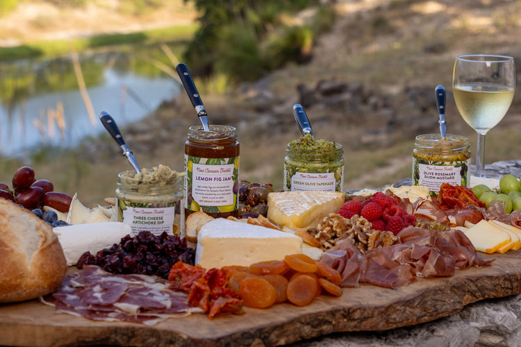 A cheese and charcuterie board by the water with Three Cheese Artichoke Dip, Lemon Fig Jam, Green Olive Tapenade and Olive Rosemary Dijon Mustard