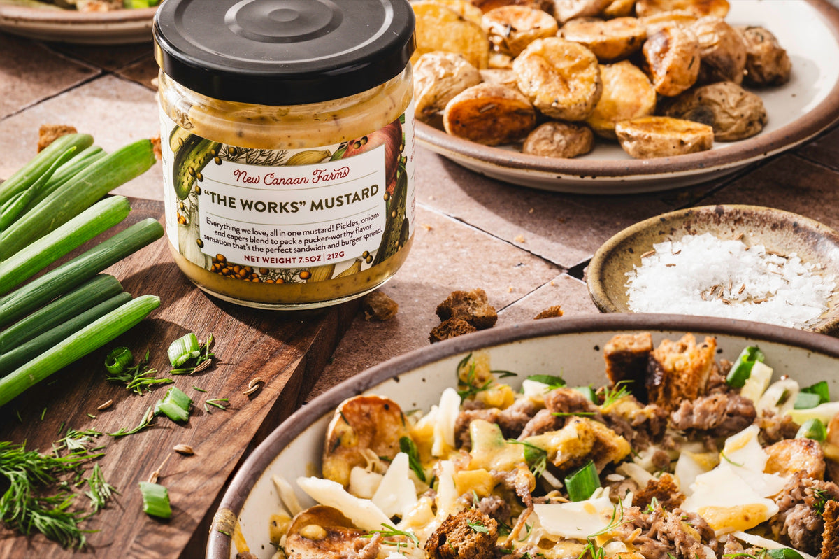 A jar of "The Works" Mustard with roasted potatoes and a potato salad