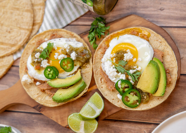Two tostadas topped with fried eggs, salsa verde, avocado and jalapeño slices