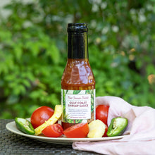 Bottle of New Canaan Farms Gulf Coast Shrimp Sauce on a plate with vegetables against a green outdoor background