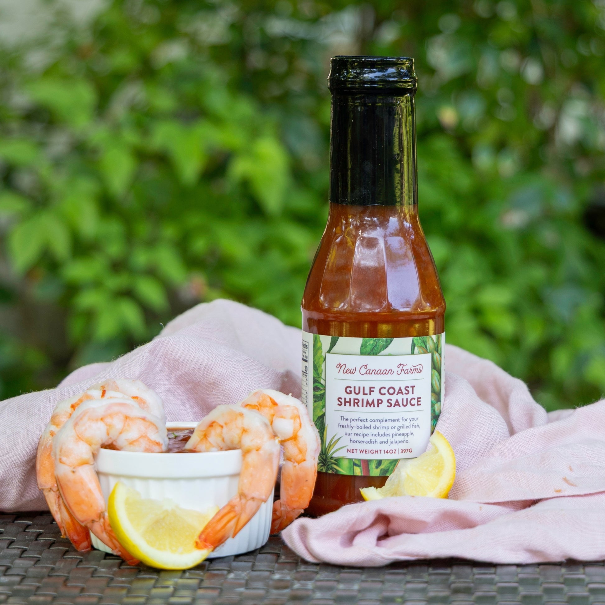 Bottle of New Canaan Farms Gulf Coast Shrimp Sauce with shrimp and lemon on a table outdoors