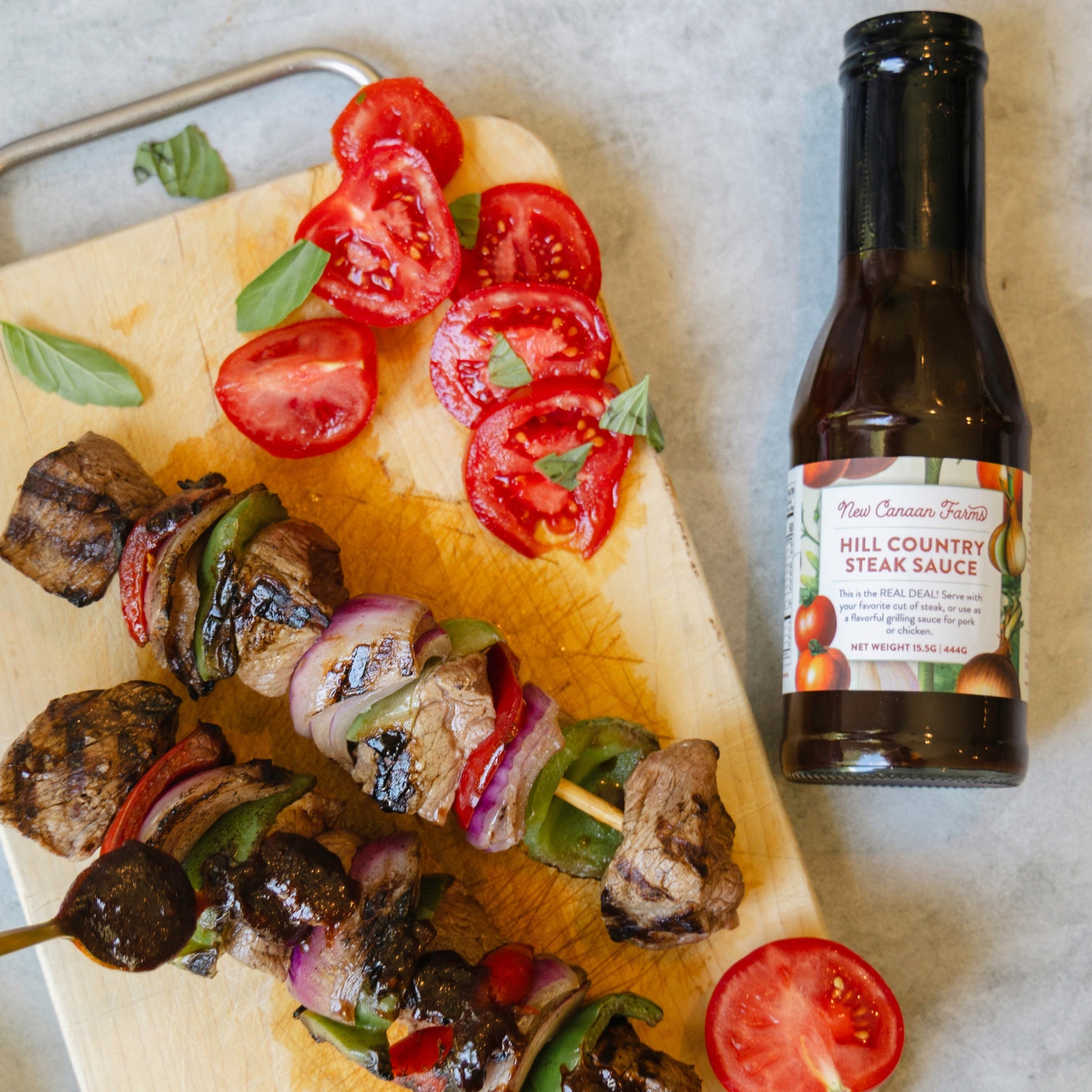 Grilled skewers with vegetables on a cutting board next to a bottle of New Canaan Farms Hill Country Steak Sauce.