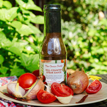 Bottle of New Canaan Farms  Hill Country Steak Sauce on a plate with tomatoes and onions outdoors