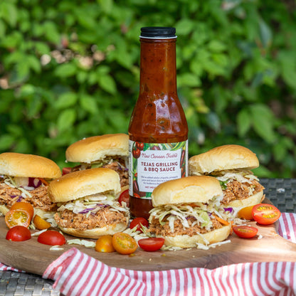 Burgers with New Canaan Farms Tejas Grilling & BBQ Sauce on a wooden board outdoors.