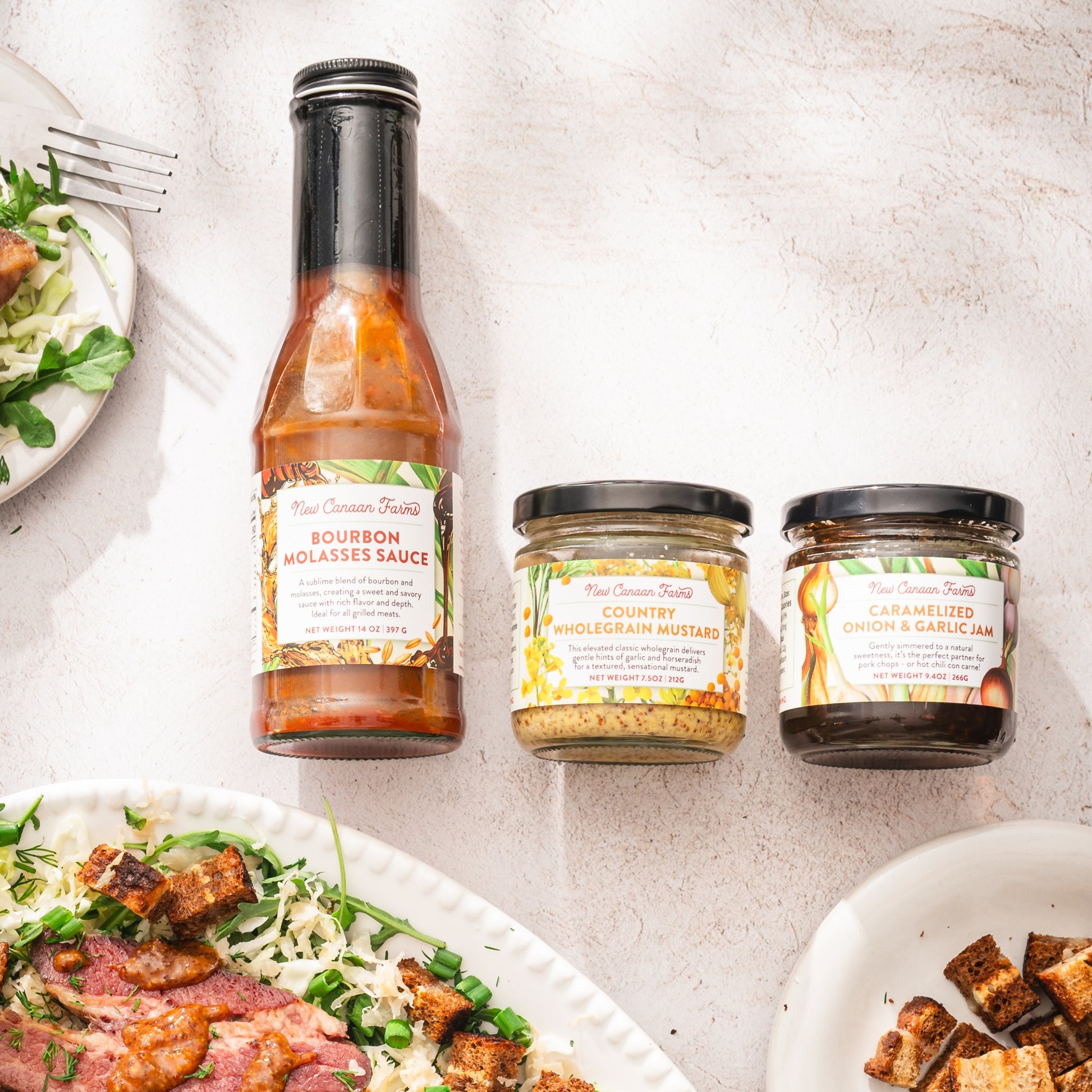 Bottle of bourbon molasses sauce and two jars on a table with plates of food.