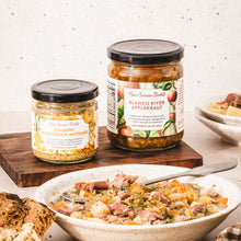 Two jars of food on a wooden board with a bowl of salad in the foreground.