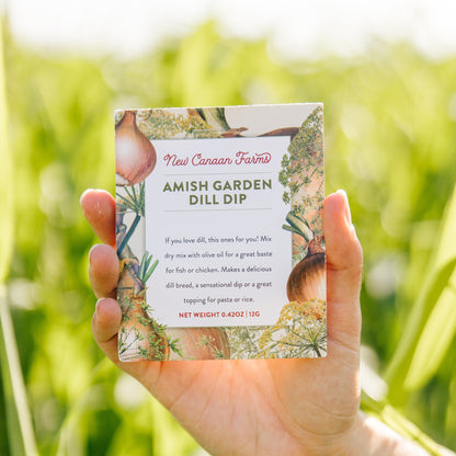 Hand holding a box of New Canaan Farms Amish Garden Dill Dip against a blurred green outdoor background