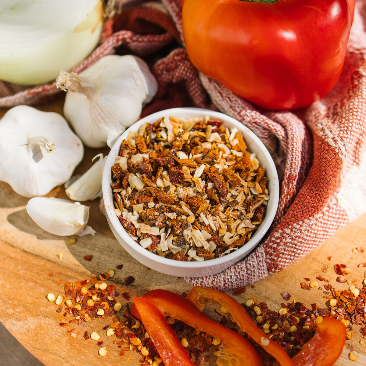 Close-up of a white bowl of Cajun Swamp Root Dip dry mix with garlic, a red pepper and red pepper flakes