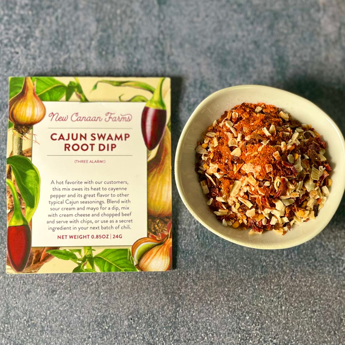 Cajun Swamp Root Dip packet next to a white bowl of the orange-red dry mix on a gray surface