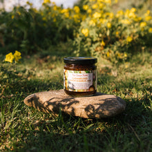 Jar of caramelized onion & garlic jam on a stone with yellow flowers in the background