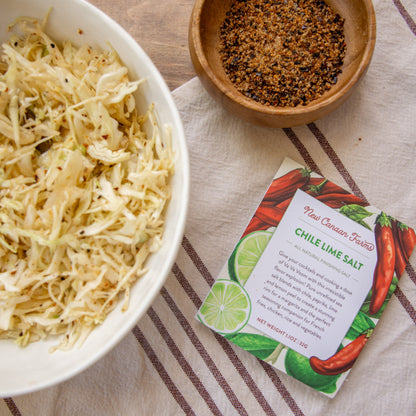 Bowl of coleslaw with a package of Chile Lime Salt seasoning on a striped tablecloth.