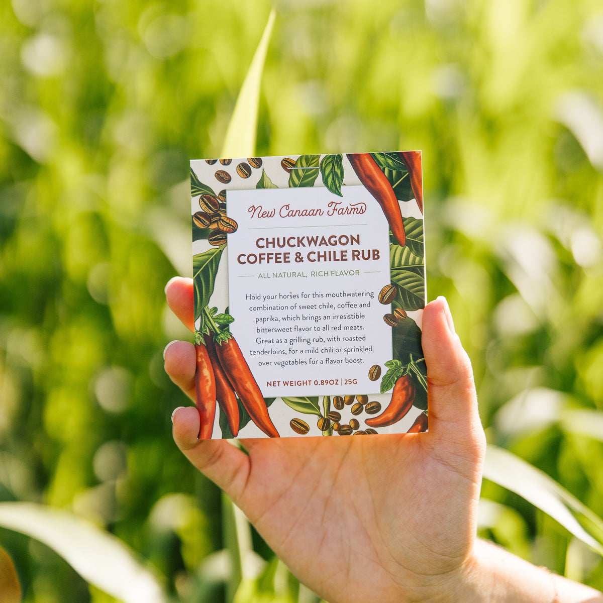 Hand holding a box of Chuckwagon Coffee & Chile Rub against a green outdoor background