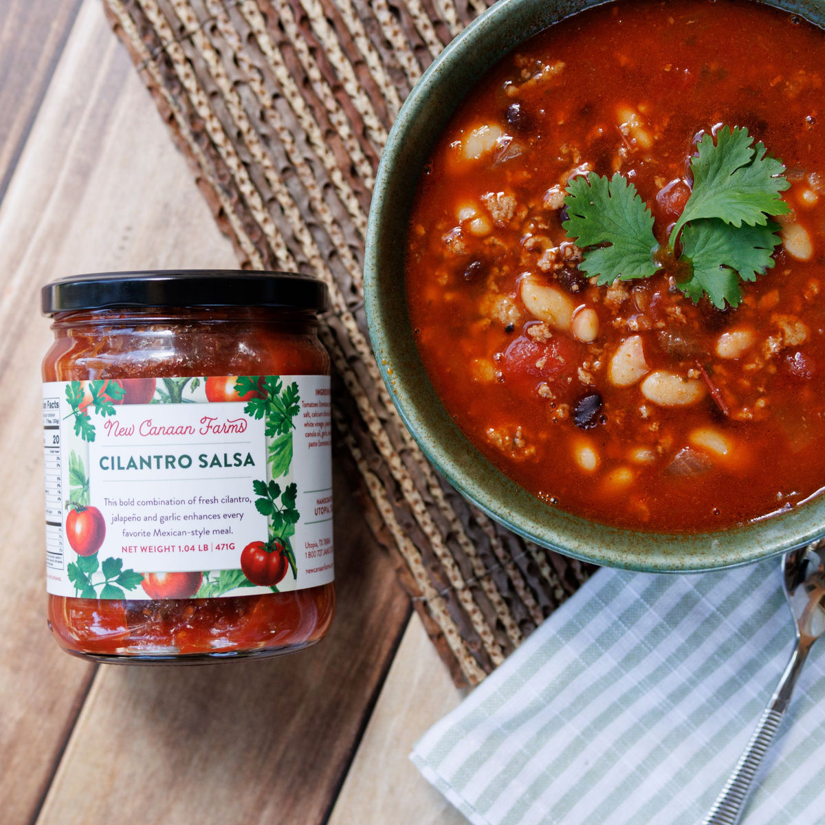 A jar of New Canaan Farms Cilantro Salsa beside a bowl of bean chili topped with a cilantro leaf