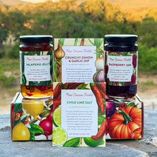 Jars of New Canaan Farms Jalapeño Jelly and Raspberry Jam sit outside on a beautiful seasonal fruits-inspired gift box, together with a New Canaan Farms Crunchy Onion & Garlic Dip mix, and a packet of Chile Lime Salt