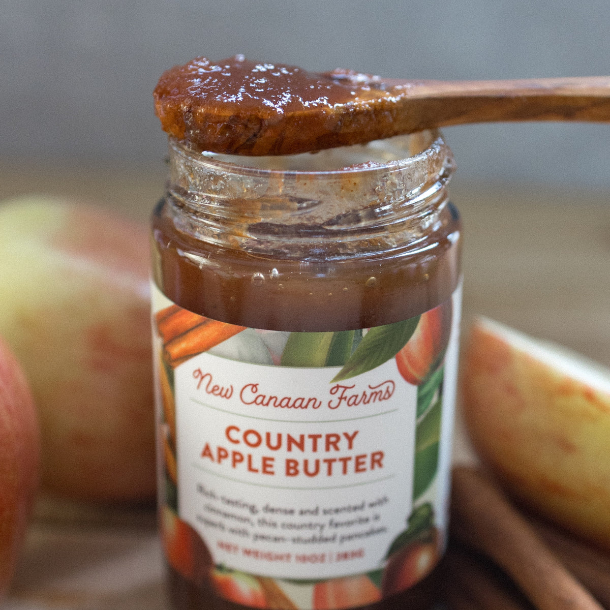 Close-up of a wooden spoon of Country Apple Butter over an open jar of New Canaan Farms Country Apple Butter