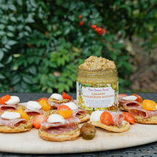 Jar of New Canaan Farms country wholegrain mustard on a platter with crackers and toppings outdoors.