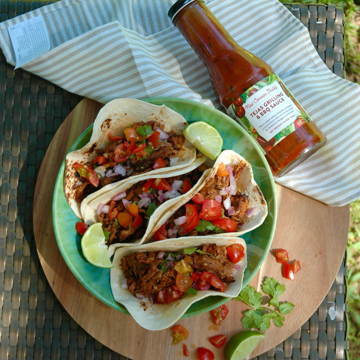 Pulled pork tacos on a plate next to a bottle of New Canaan Farms Tejas Grilling & BBQ Sauce