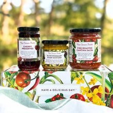 Jars of New Canaan Farms Cherry Preserves, Fire-Roasted Cantina Salsa and Olive Rosemary Dijon Mustard displayed on top of a colorful vegetable-inspired gift box outside