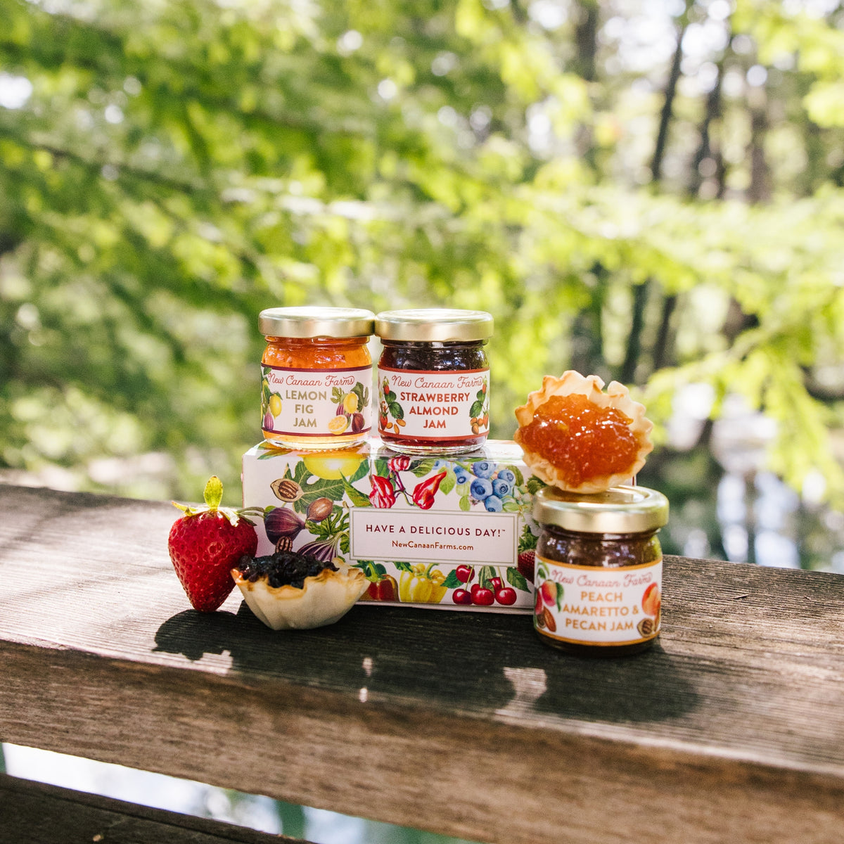 Jars of jam and a box with fruit illustrations on a wooden surface outdoors.