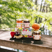 Jars of jam and a box with fruit illustrations on a wooden surface outdoors.