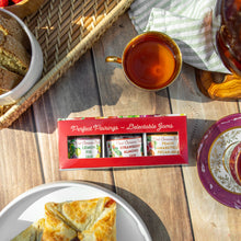 Tea cup with a box of Perfect Pairings jams on a wooden table with pastries and bread.