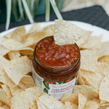 Jar of New Canaan Farms salsa with a tortilla chip on top, surrounded by tortilla chips on a white plate.