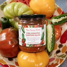 Jar of New Canaan Farms Fire-Roasted Cantina Salsa surrounded by fresh tomatoes and jalapeños on a decorative plate.