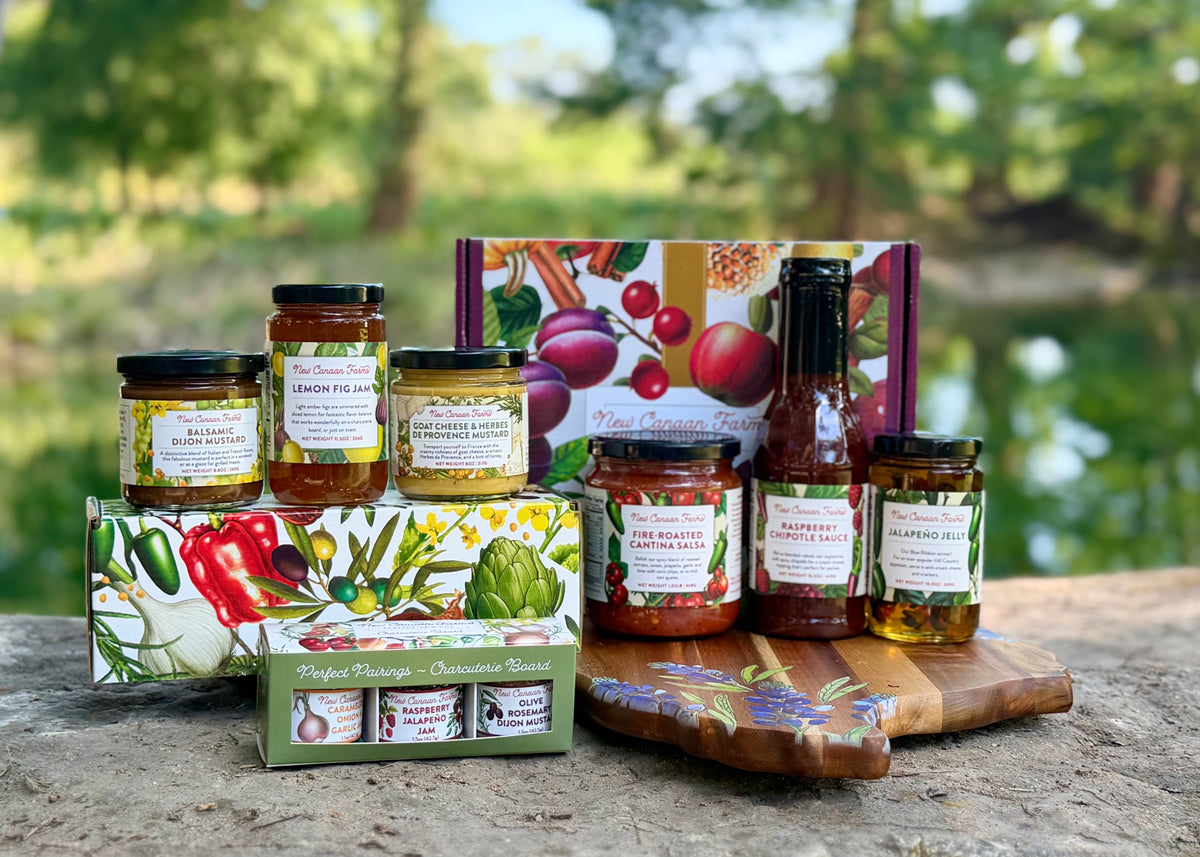 New Canaan Farms gift boxes with jars of mustard, jam, salsa and Raspberry Chipotle Sauce on a rock above a river