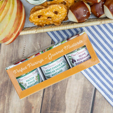Box of New Cannelle mustards with pretzels, apples, and a striped cloth on a wooden surface