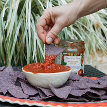 Hand dipping a tortilla chip into a bowl of salsa with a New Canaan Farms Habanero salsa jar in the background.