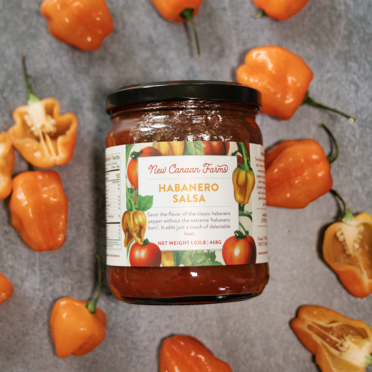 Jar of New Canaan Farms Habanero Salsa surrounded by habanero peppers on a gray background
