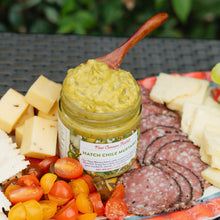 Jar of New Canaan Farms Hatch Chile Mustard on a charcuterie board with cheese, salami, and tomatoes.