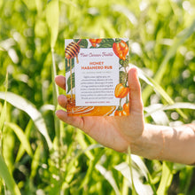 Hand holding a package of Honey Habanero Rub in front of green foliage