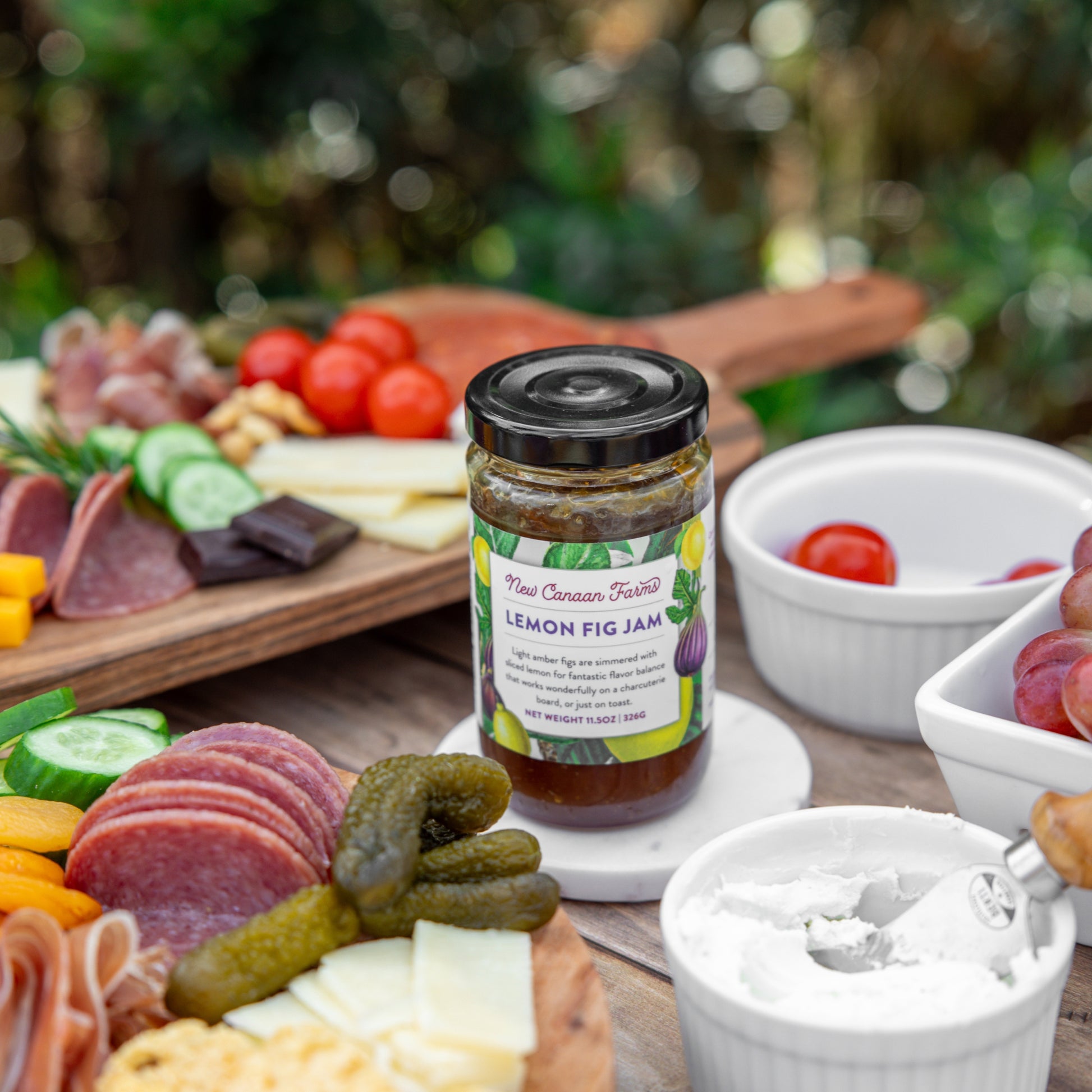 Jar of lemon fig jam on a charcuterie board with various meats, cheeses, and fruits.