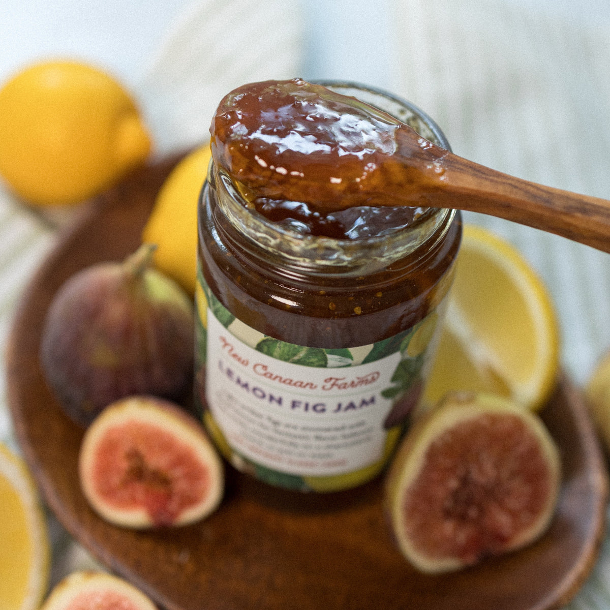 Wooden spoon of Lemon Fig Jam resting on the jar, with fresh figs and lemons on a wooden plate