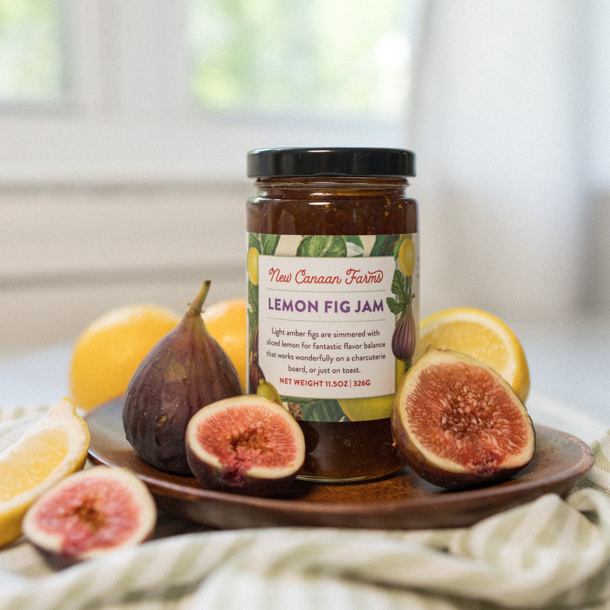 New Canaan Farms Lemon Fig Jam on a wooden plate with halved fresh figs and lemon wedges
