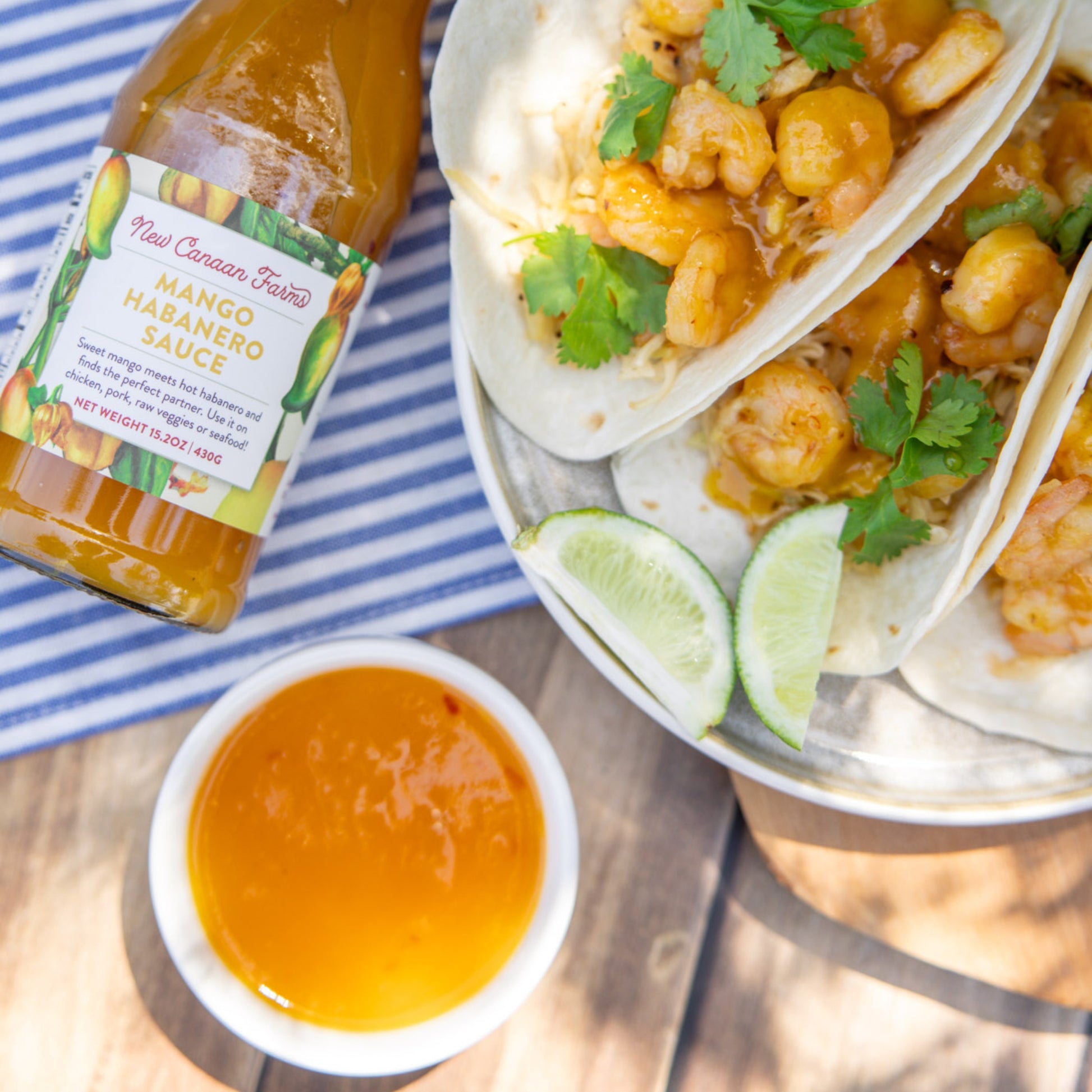 Mango habanero sauce bottle with tacos and lime wedges on a striped cloth