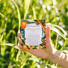 Hand holding a package of New Canaan Farms Merry Mulling Spice against a green field background
