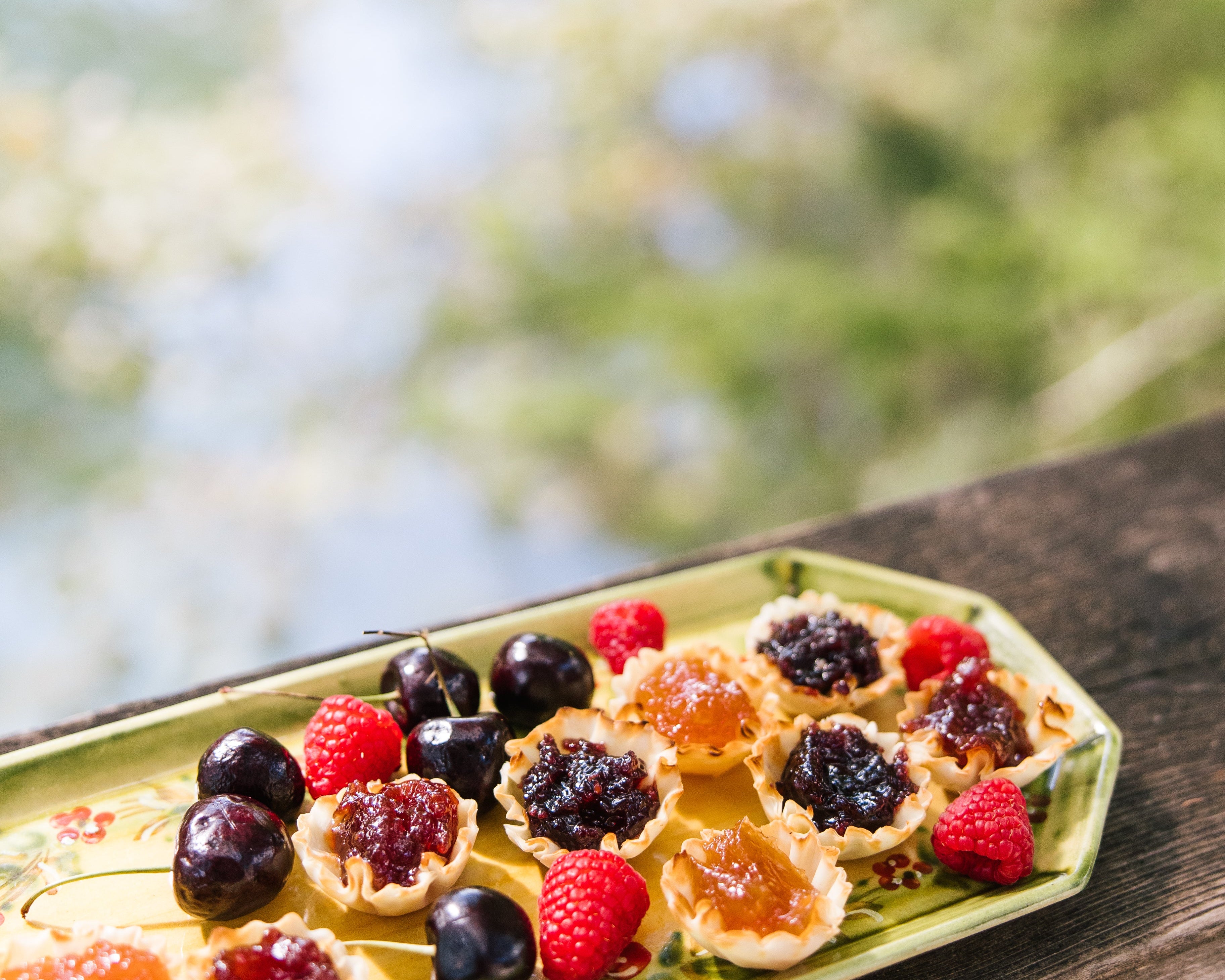 Small pastries with fruit toppings on a green plate outdoors