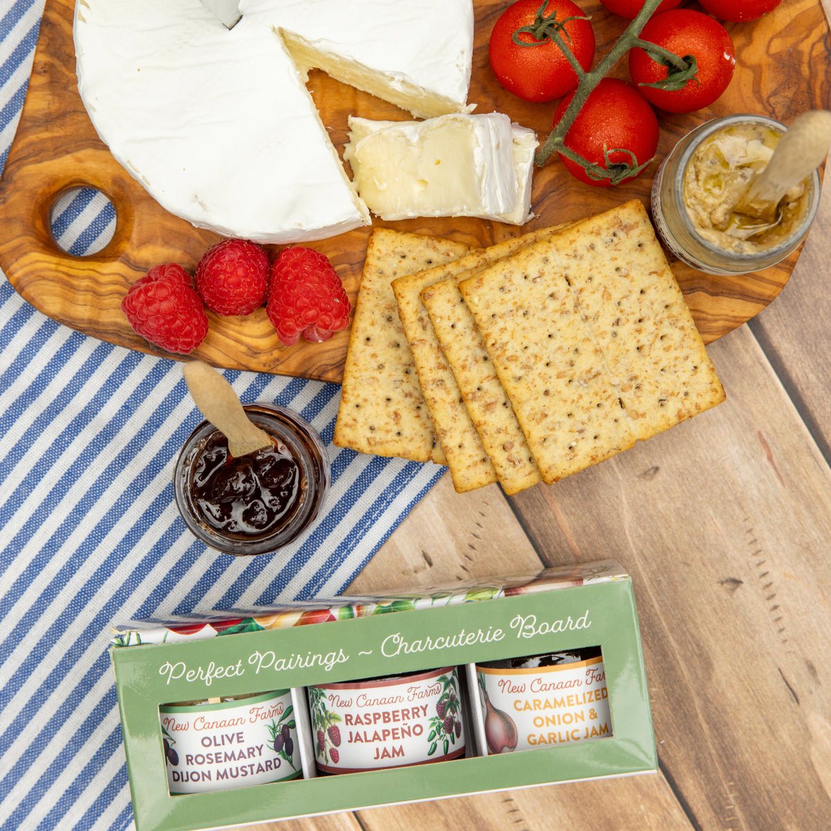Perfect Pairings Charcuterie Board box beside a board of brie, crackers, raspberries, tomatoes and a jar of jam