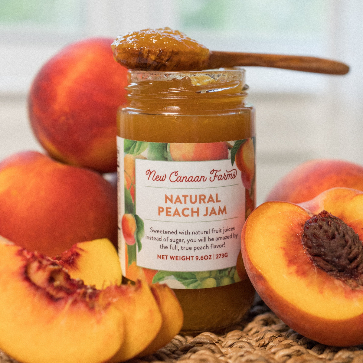 New Canaan Farms Natural Peach Jam jar with a spoonful on top, surrounded by fresh peaches