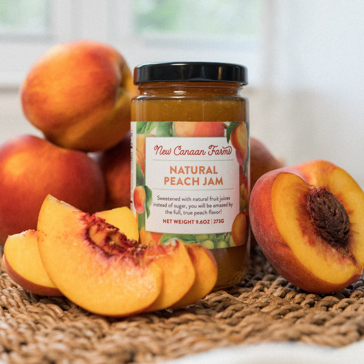 New Canaan Farms Natural Peach Jam jar beside peach slices and a halved peach on a woven mat