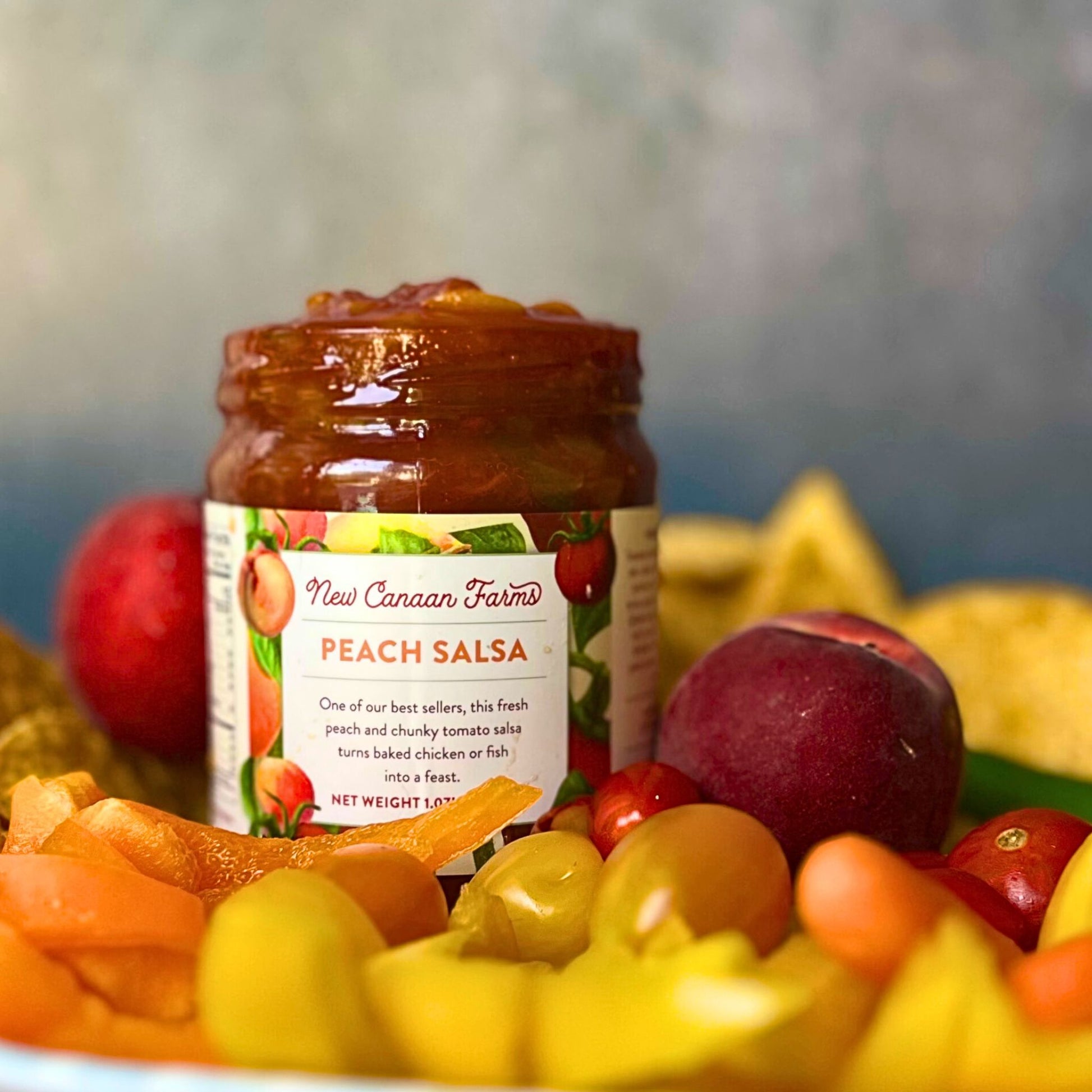 Jar of New Canaan Farms Peach Salsa surrounded by peaches and salsa on a blurred background