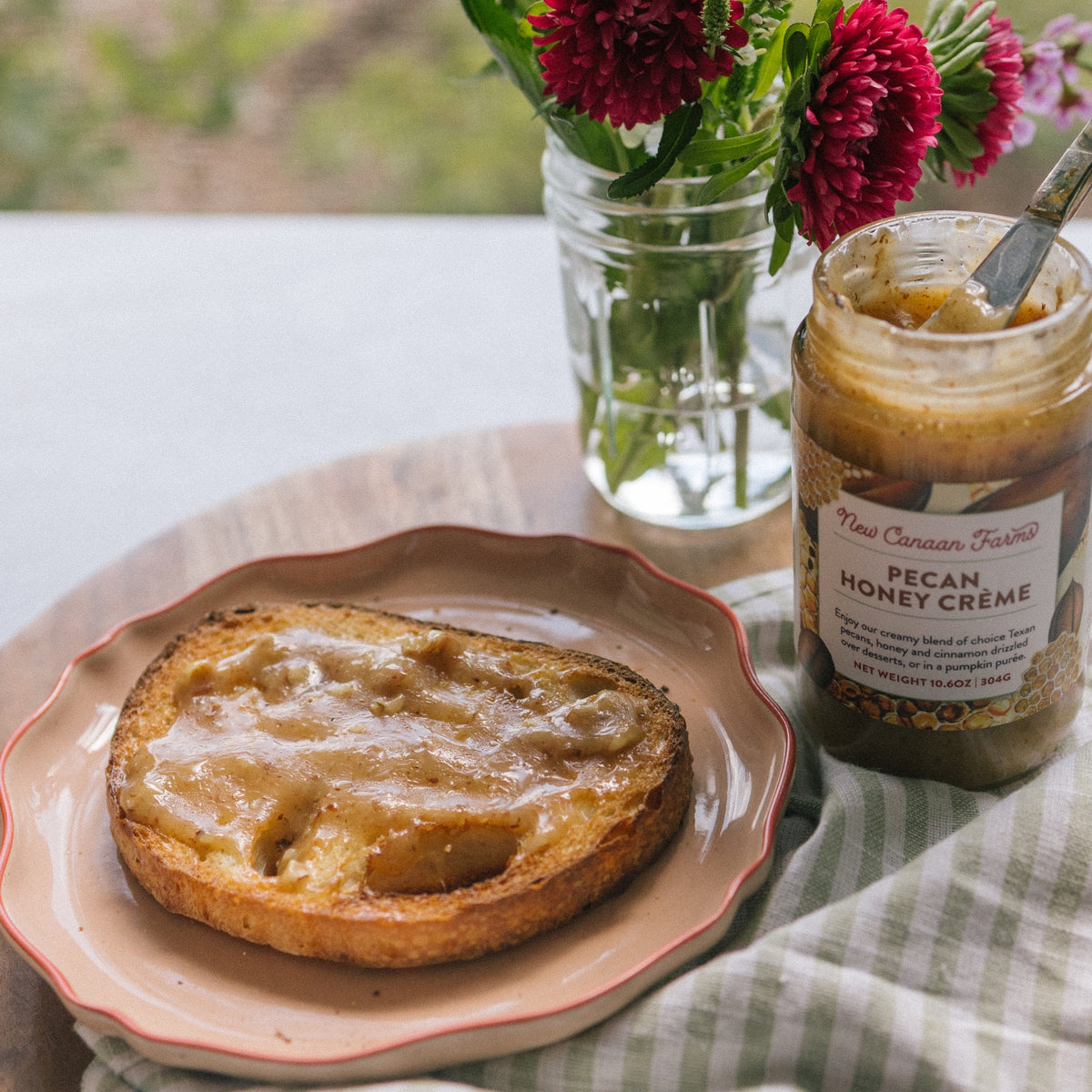 Toast spread with Pecan Honey Crème on a plate, beside an open jar of New Canaan Farms Pecan Honey Crème