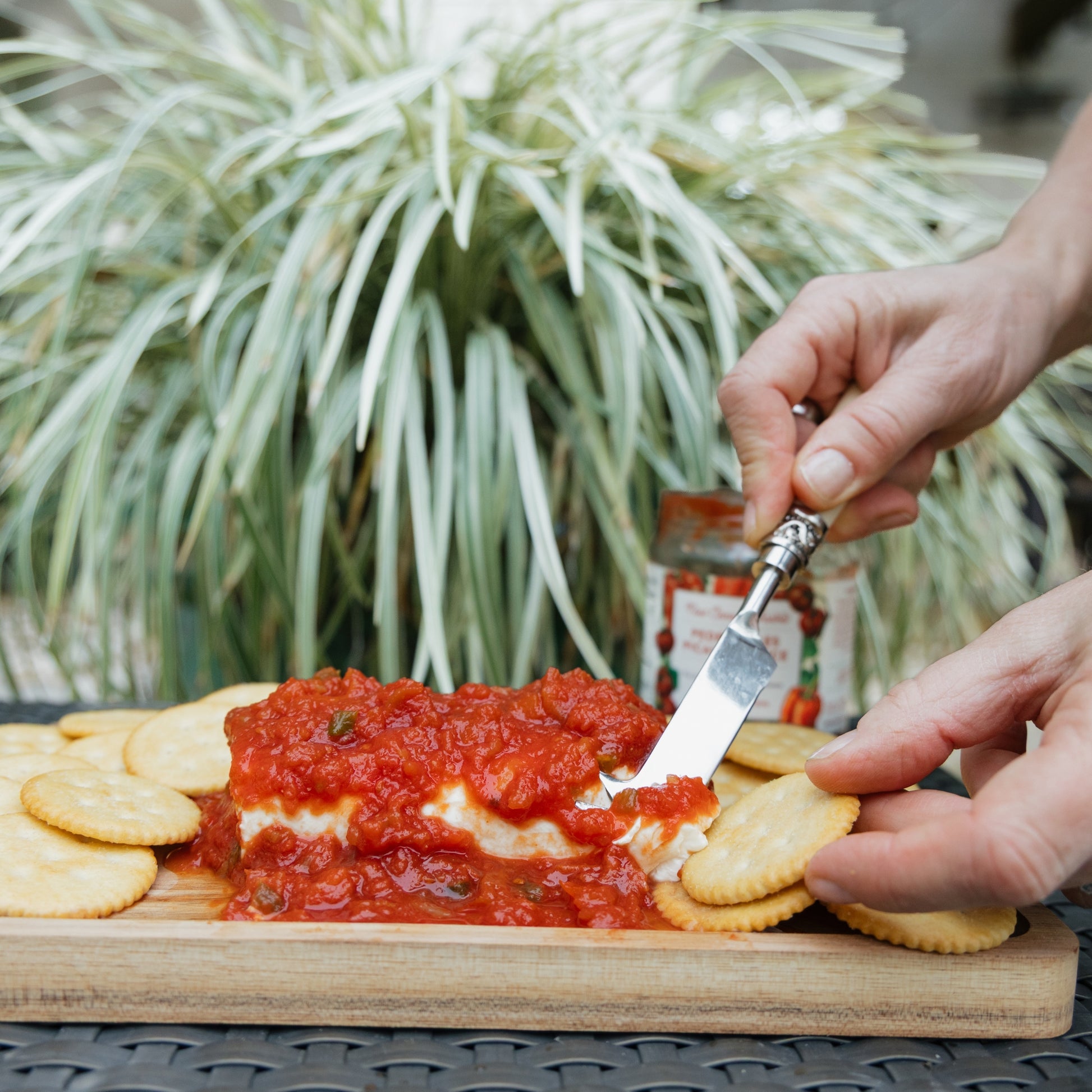 Person spreading New Canaan Farms Pedernales Picante Sauceon crackers with a knife