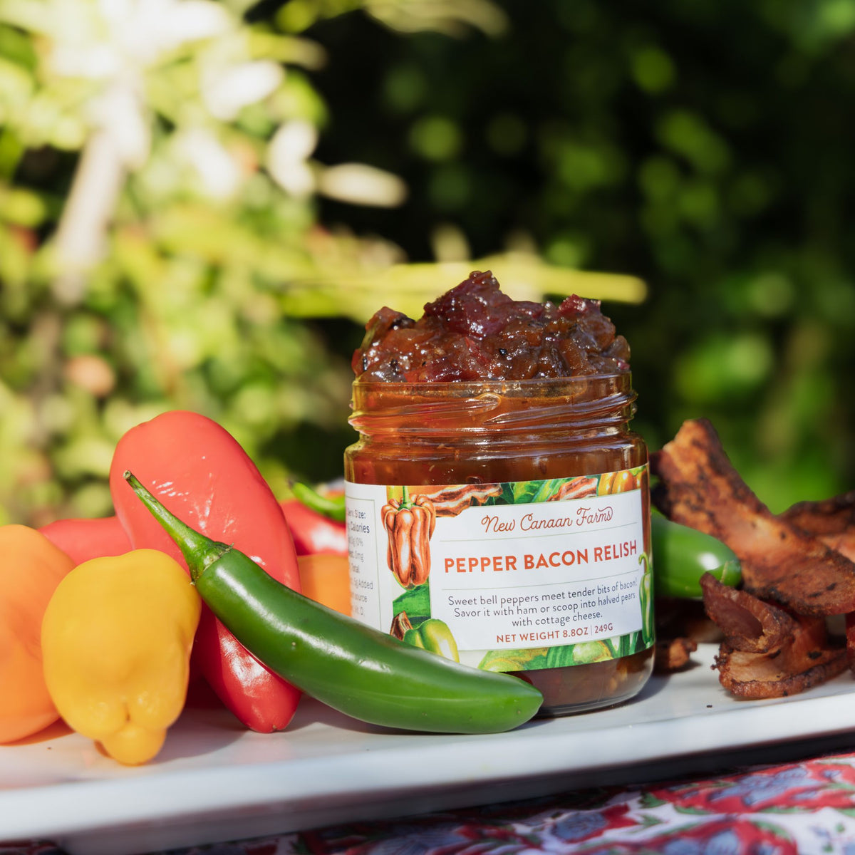 Jar of pepper bacon relish with peppers and meat on a plate outdoors