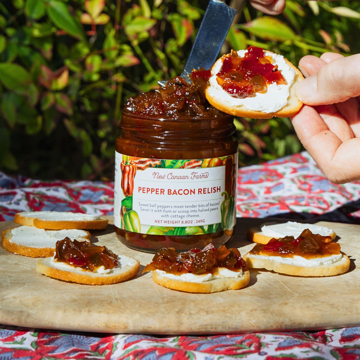 Jar of pepper bacon relish with crackers on a wooden board outdoors