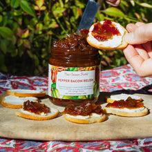 Jar of pepper bacon relish with crackers on a wooden board outdoors